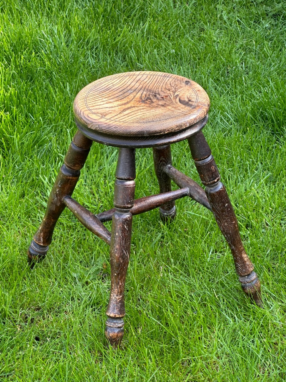 A 19th-century rustic wooden stool featuring a circular solid elm seat and four dark turned splayed legs with stretchers. View IV
