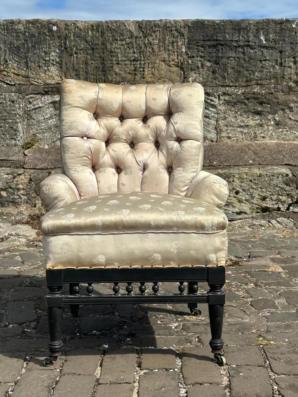 A Victorian button-back drawing room chair with cream damask upholstery, ebonised turned legs, a spindled stretcher gallery, and brass casters. View IV
