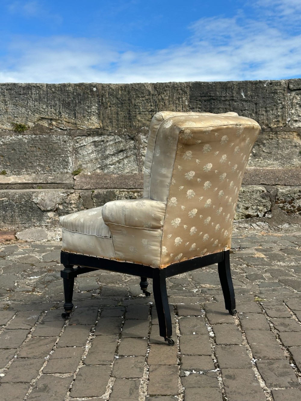 A Victorian button-back drawing room chair with cream damask upholstery, ebonised turned legs, a spindled stretcher gallery, and brass casters. View VI