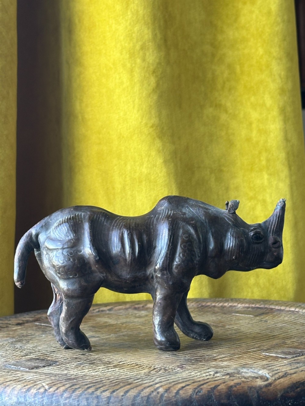 A small moulded dark brown leather rhinoceros desk ornament with textured hide detailing and hand-stitched seams standing on a wooden surface. View II