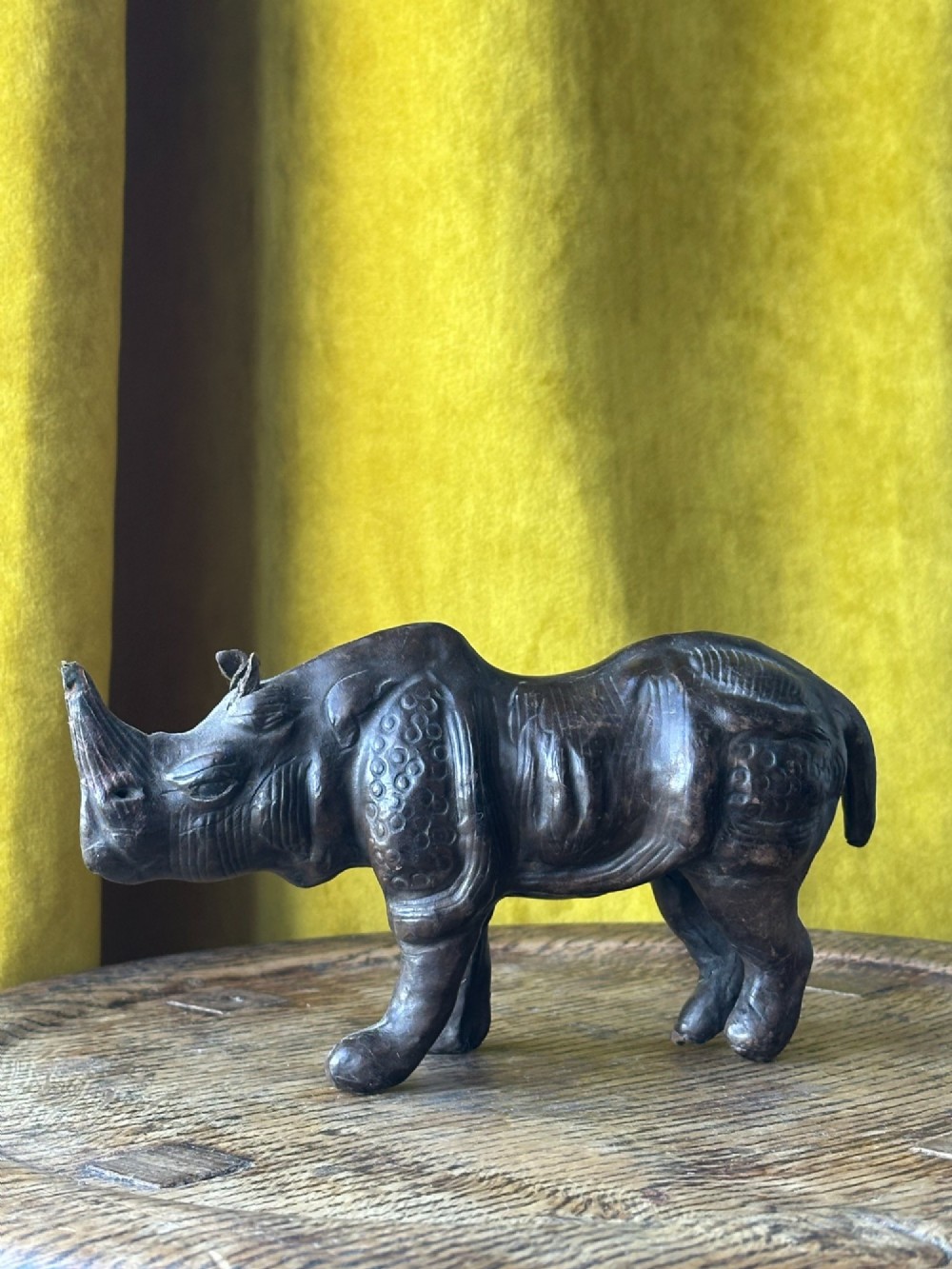 A small moulded dark brown leather rhinoceros desk ornament with textured hide detailing and hand-stitched seams standing on a wooden surface.