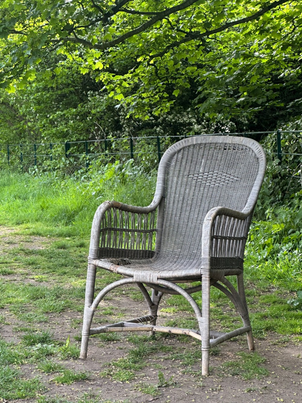 An early 20th-century handwoven cane armchair featuring a high backrest, openwork arms, and curved structural stretchers in weathered grey.