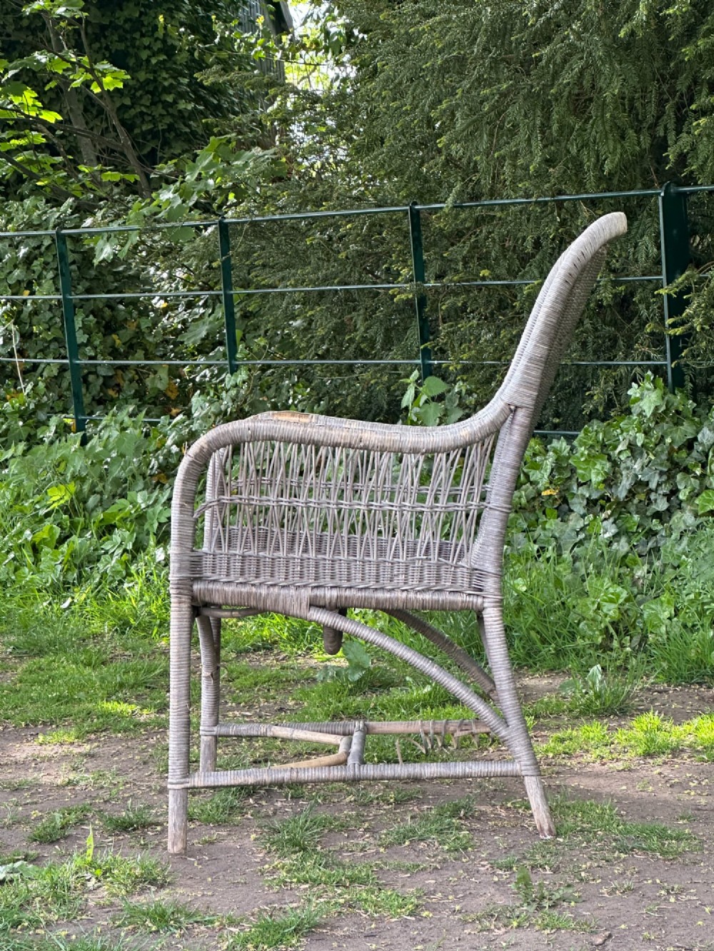 An early 20th-century handwoven cane armchair featuring a high backrest, openwork arms, and curved structural stretchers in weathered grey. View IV