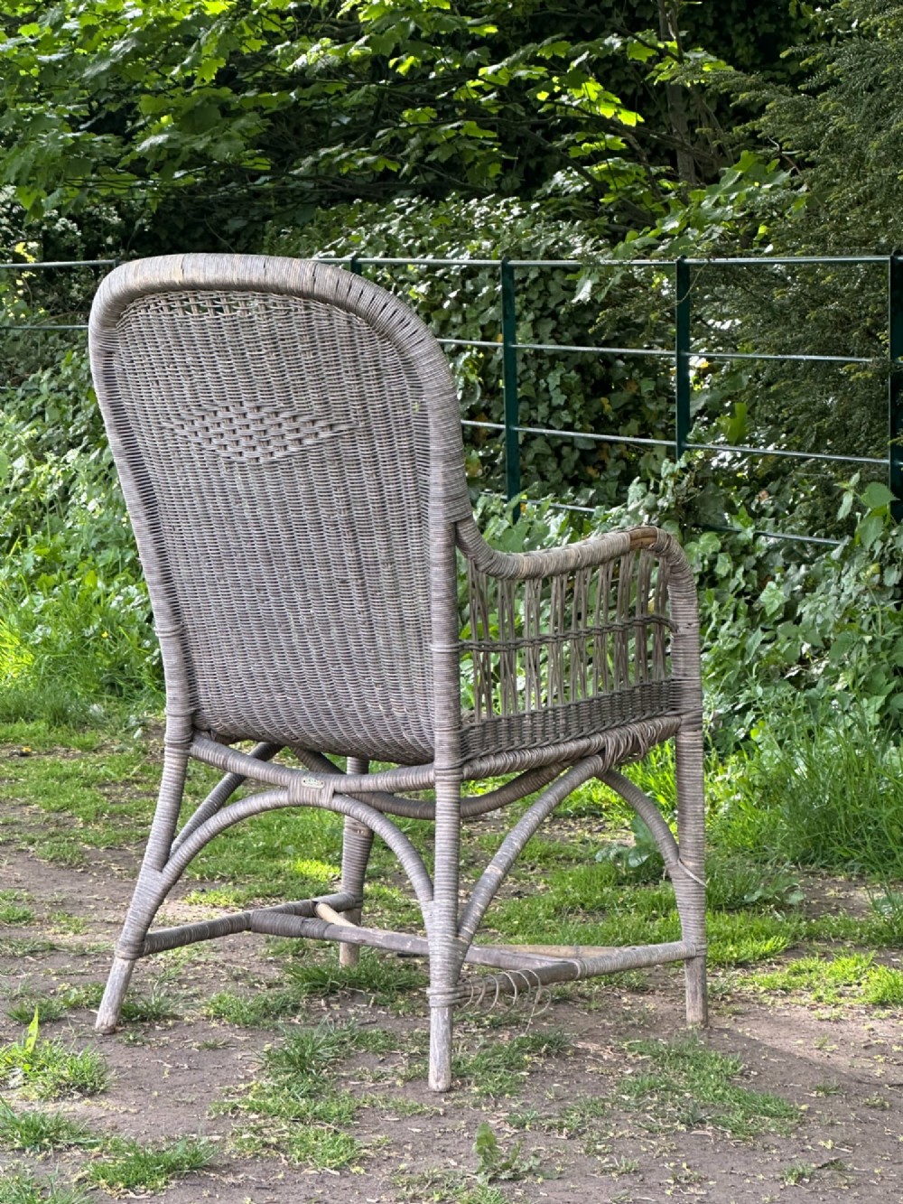 An early 20th-century handwoven cane armchair featuring a high backrest, openwork arms, and curved structural stretchers in weathered grey. View V