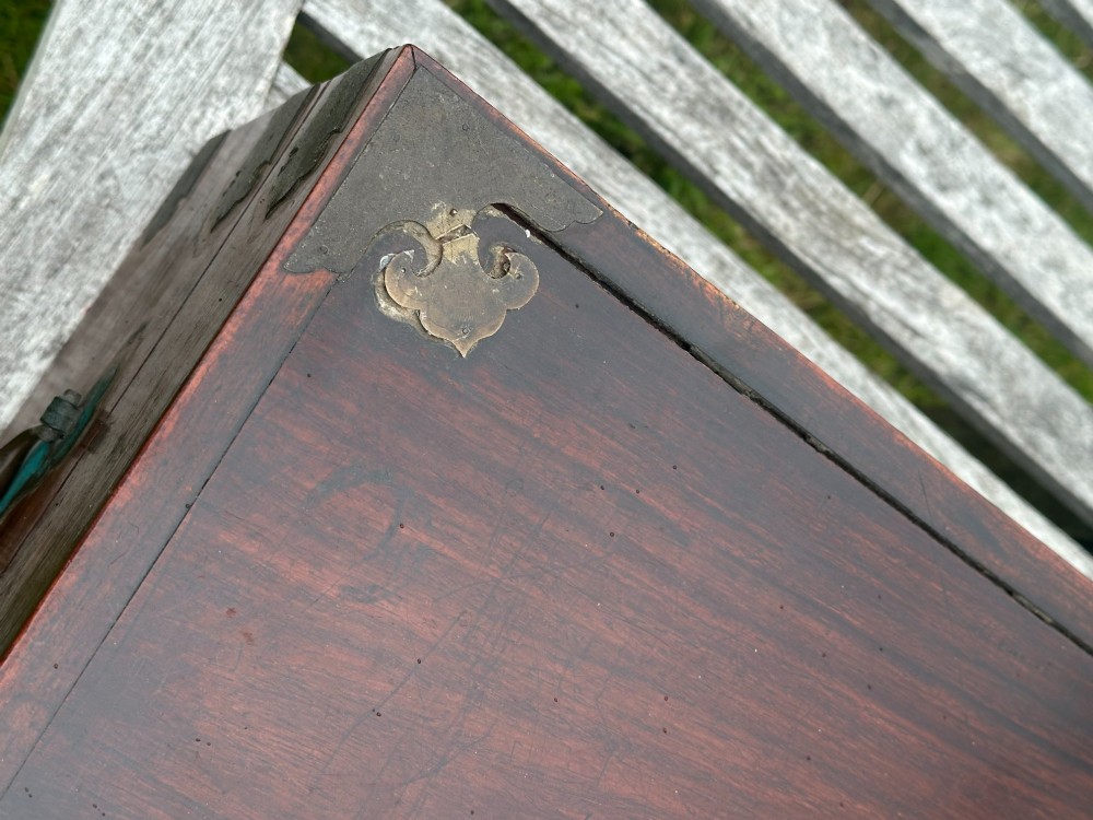 A rectangular reddish-brown padouk wood deed box featuring brass corner mounts, a central keyhole escutcheon, and brass side carrying handles. View VI