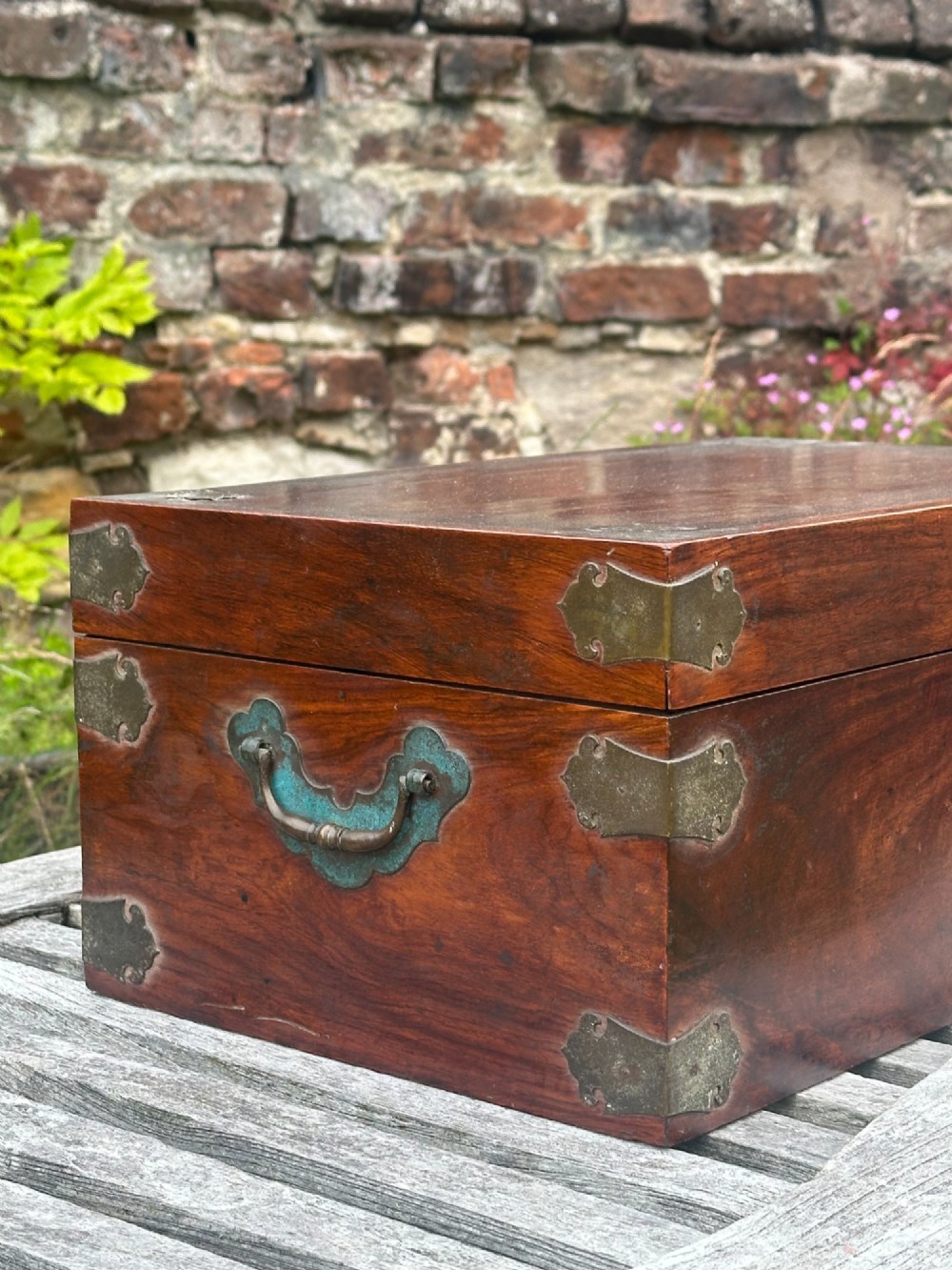 A rectangular reddish-brown padouk wood deed box featuring brass corner mounts, a central keyhole escutcheon, and brass side carrying handles. View VII