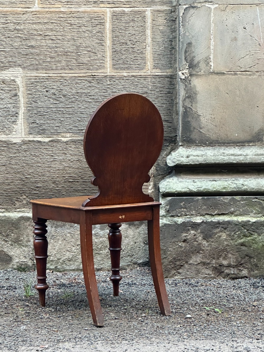 Victorian carved oak hall chair featuring a round carved backrest with a central shield motif, turned front legs, and a solid wooden seat. View II