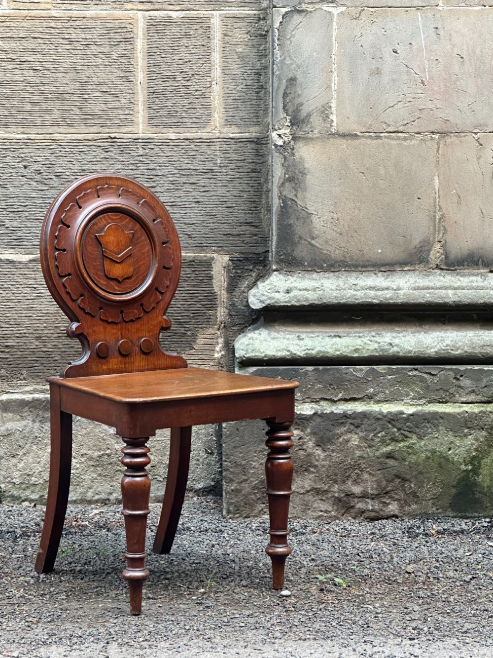 Victorian carved oak hall chair featuring a round carved backrest with a central shield motif, turned front legs, and a solid wooden seat.