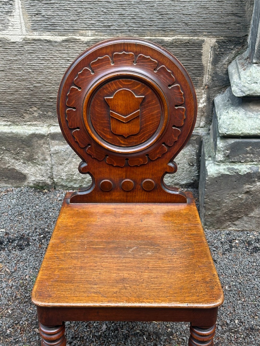 Victorian carved oak hall chair featuring a round carved backrest with a central shield motif, turned front legs, and a solid wooden seat. View III