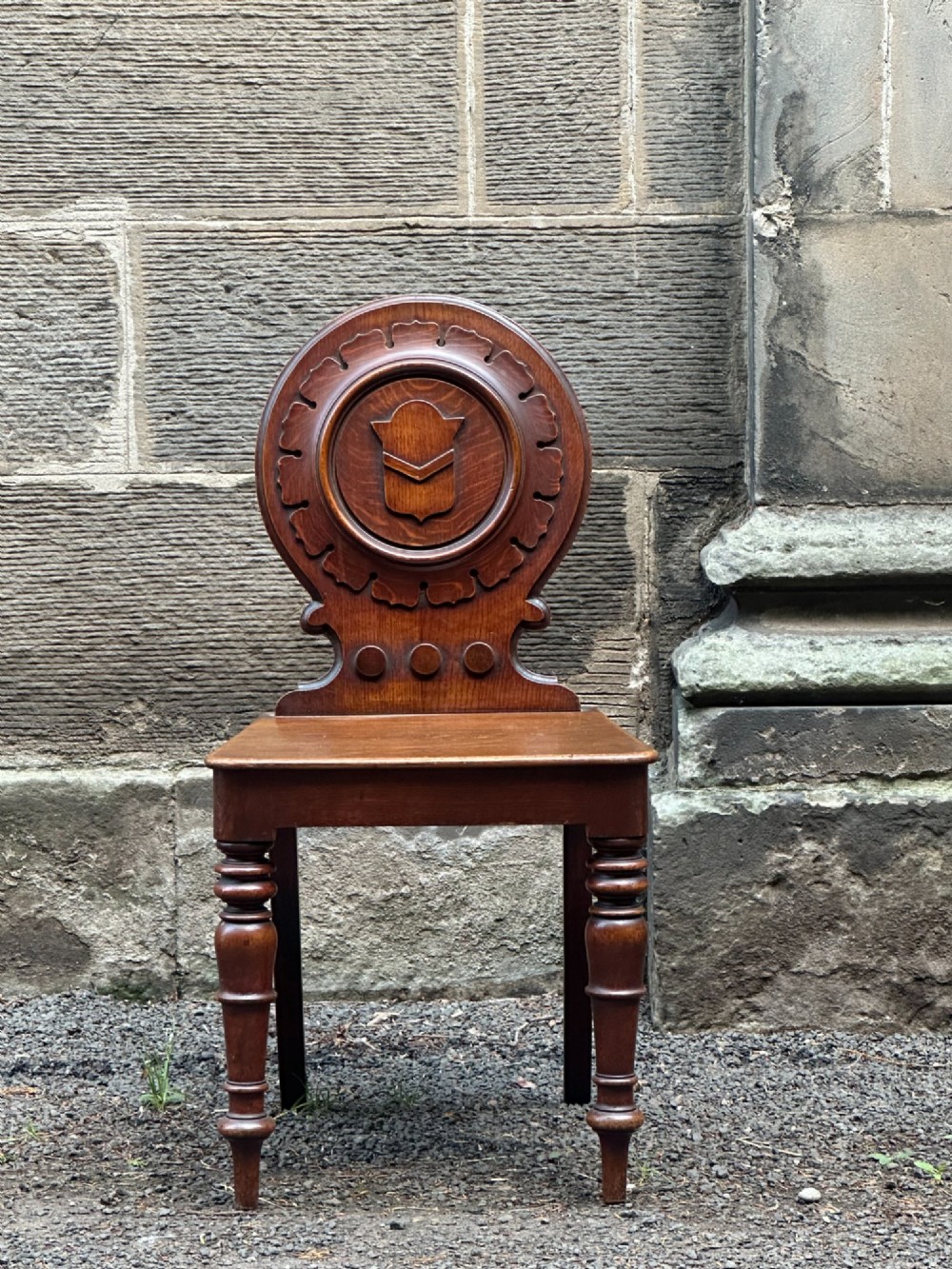 Victorian carved oak hall chair featuring a round carved backrest with a central shield motif, turned front legs, and a solid wooden seat. View IV