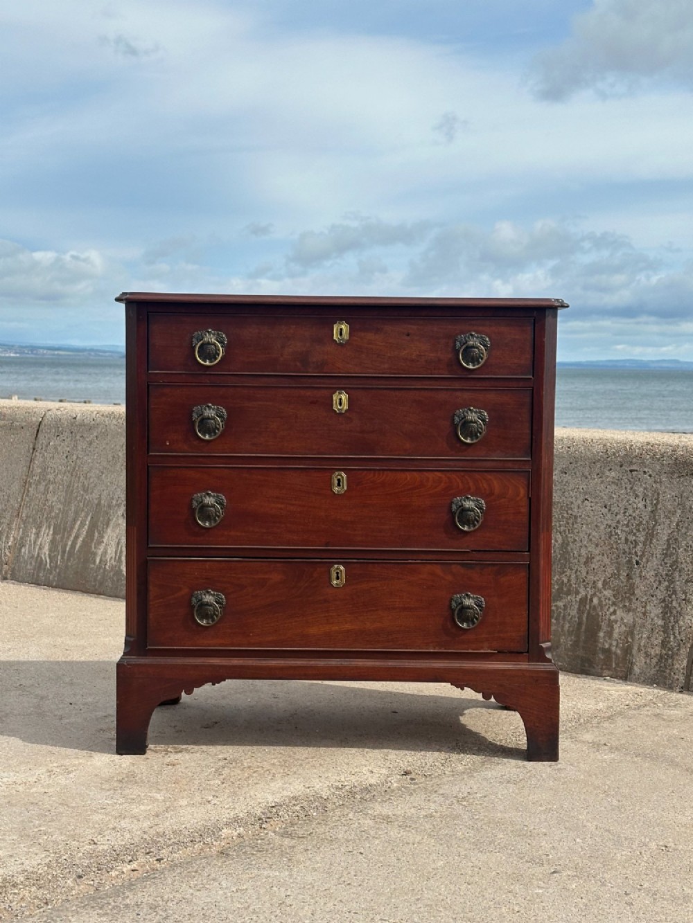 A late eighteenth-century George III mahogany chest of drawers with four graduating drawers, brass ring handles, keyhole escutcheons, and bracket feet. View II