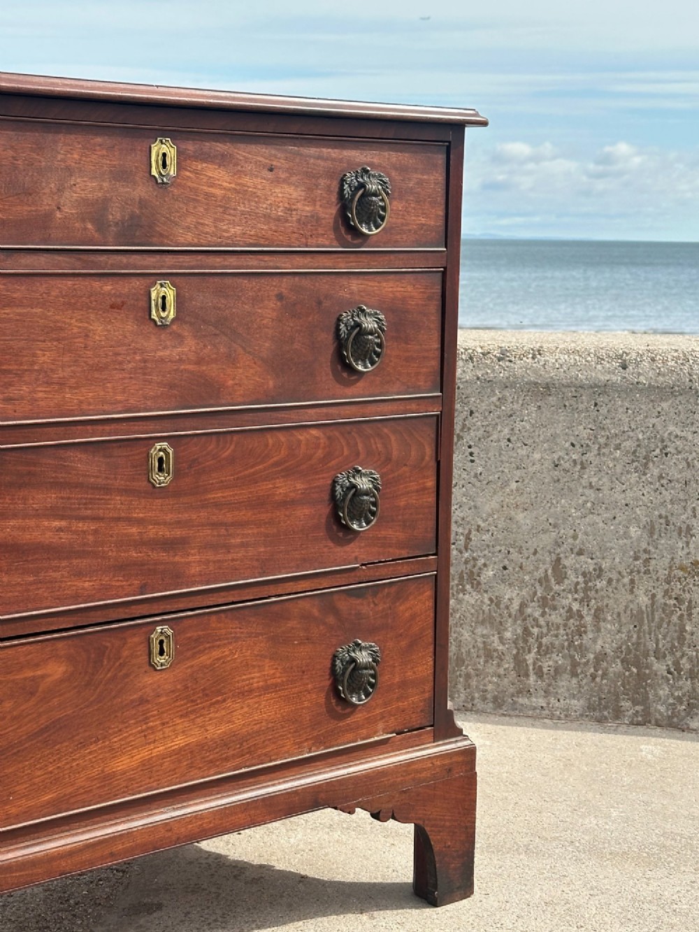 A late eighteenth-century George III mahogany chest of drawers with four graduating drawers, brass ring handles, keyhole escutcheons, and bracket feet. View VI