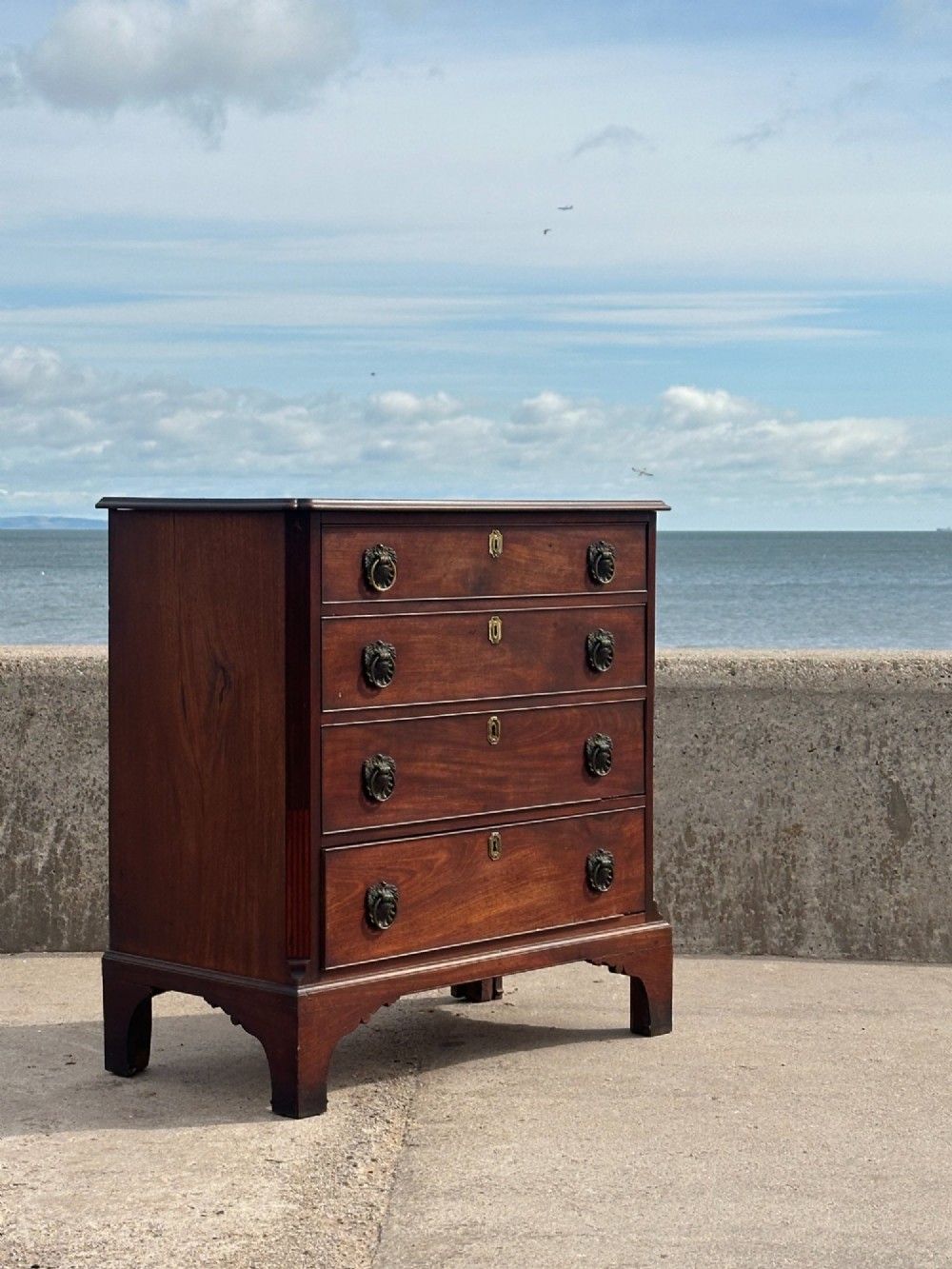 A late eighteenth-century George III mahogany chest of drawers with four graduating drawers, brass ring handles, keyhole escutcheons, and bracket feet.