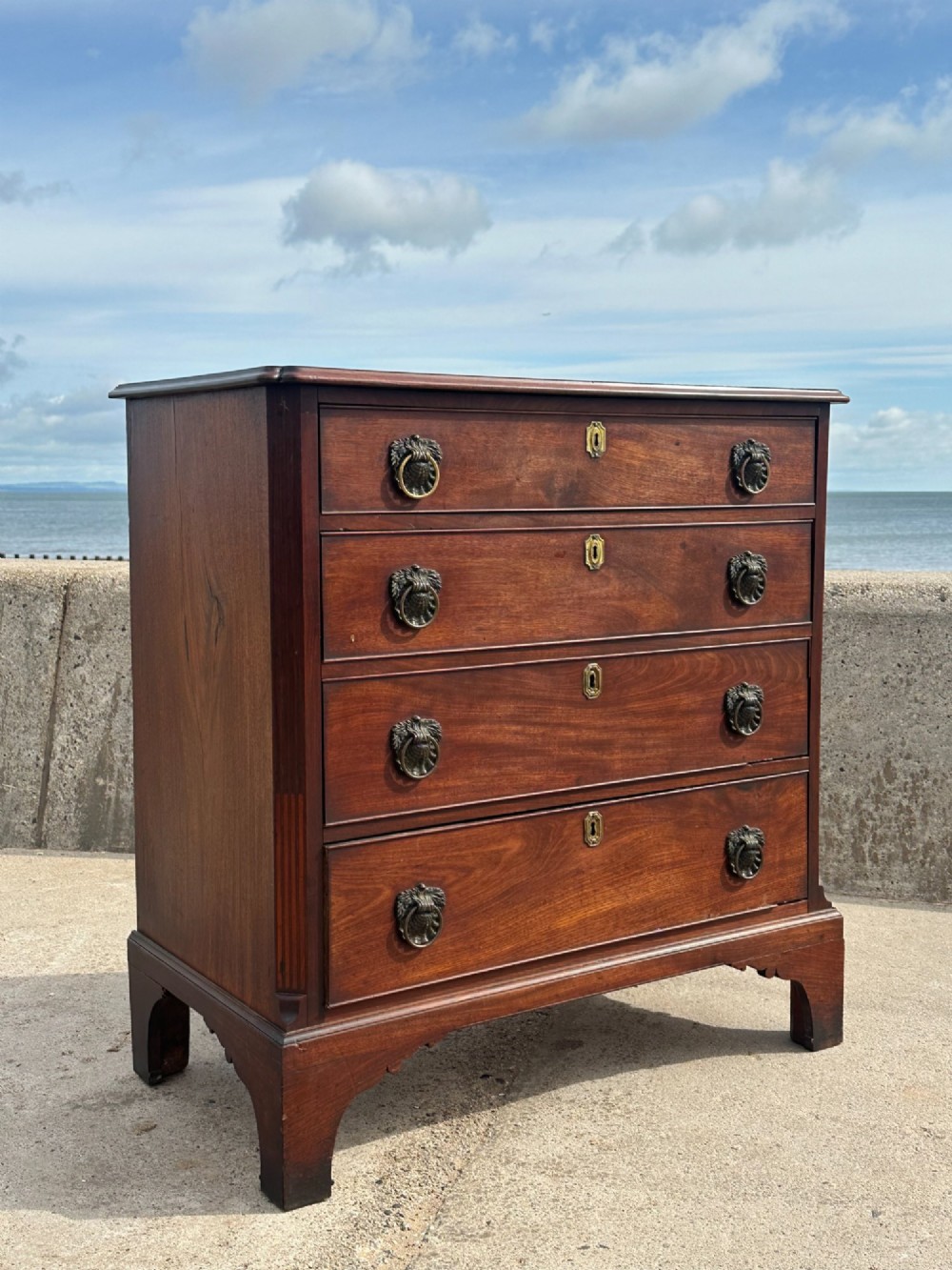 A late eighteenth-century George III mahogany chest of drawers with four graduating drawers, brass ring handles, keyhole escutcheons, and bracket feet. View VII