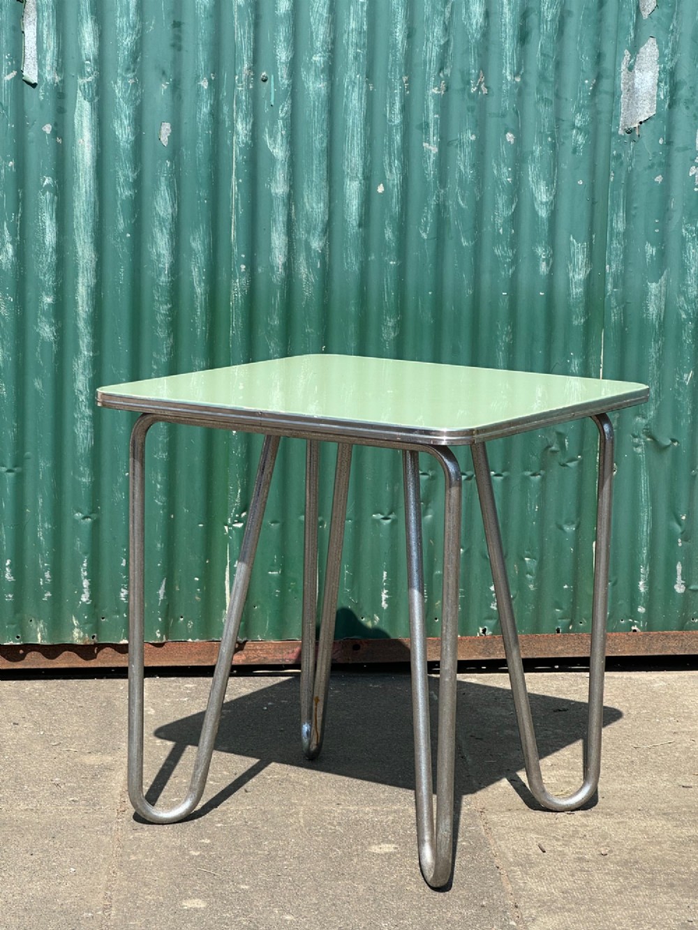 A 1930s Art Deco side table with a sage green rectangular top supported by continuous chrome tubular steel legs.