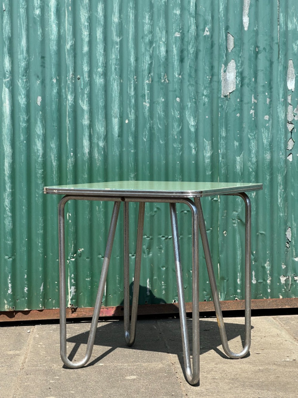 A 1930s Art Deco side table with a sage green rectangular top supported by continuous chrome tubular steel legs. View VI