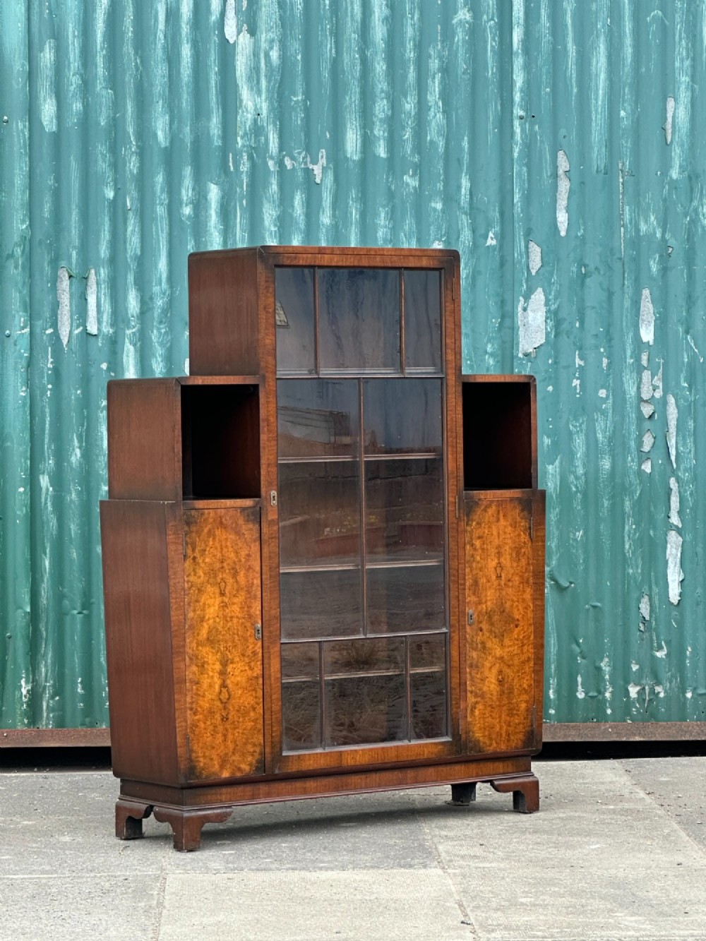 An architectural 1930s Art Deco cabinet made of warm brown walnut wood with a tall central glazed door flanked by lower cupboard doors and open alcoves. View IV