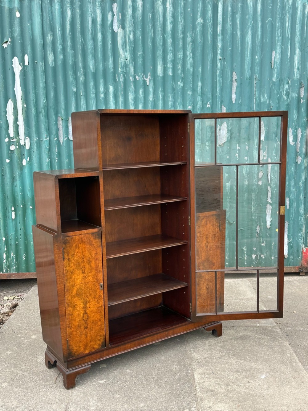 An architectural 1930s Art Deco cabinet made of warm brown walnut wood with a tall central glazed door flanked by lower cupboard doors and open alcoves. View VI