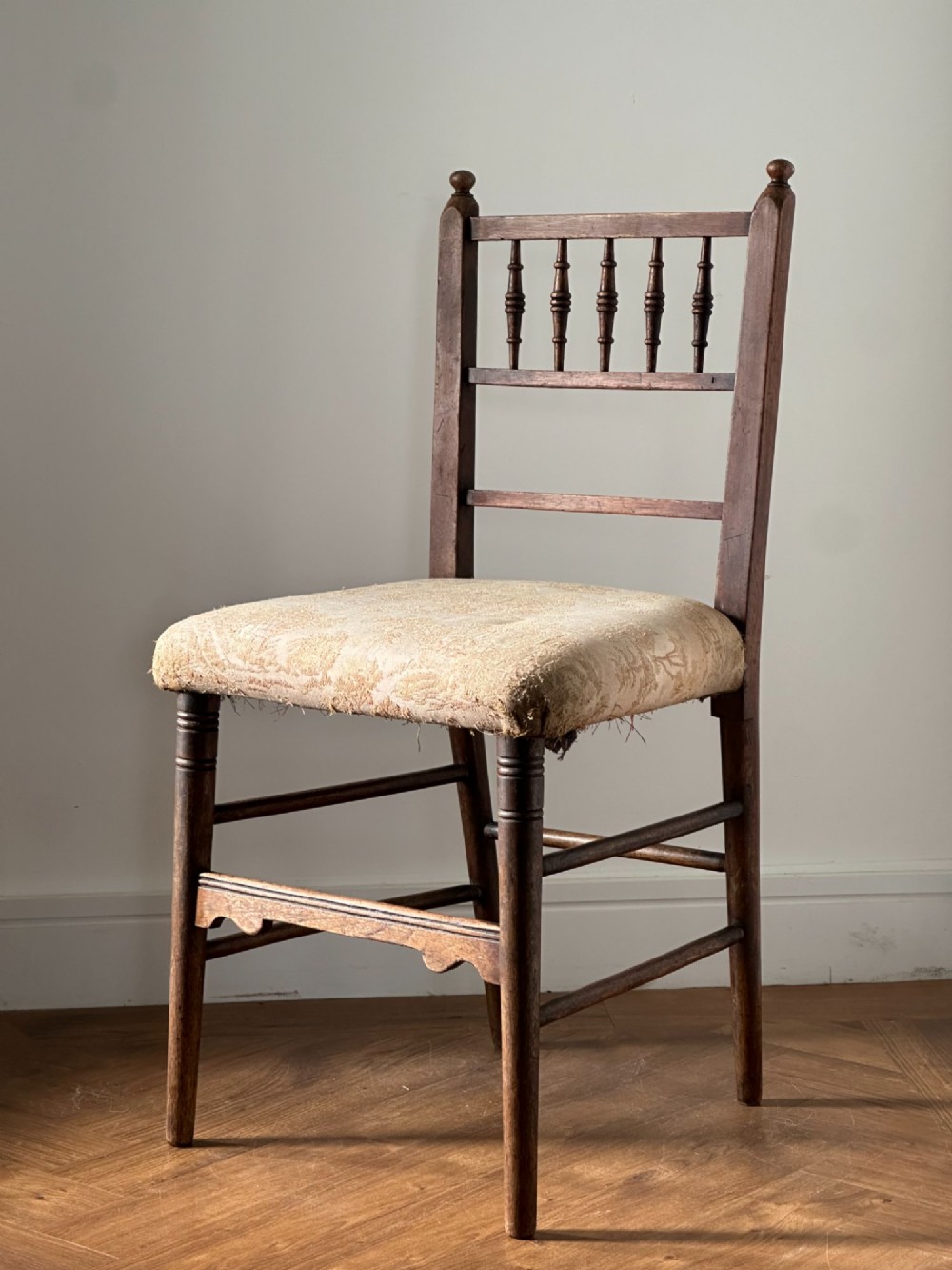 A 19th-century Sussex style side chair featuring turned spindles in the backrest, a dark wood frame, and a padded upholstered seat.