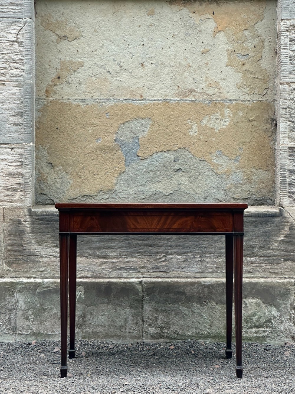 A George III mahogany side table with tapered legs, a flame mahogany veneered frieze, and a brass drawer pull.