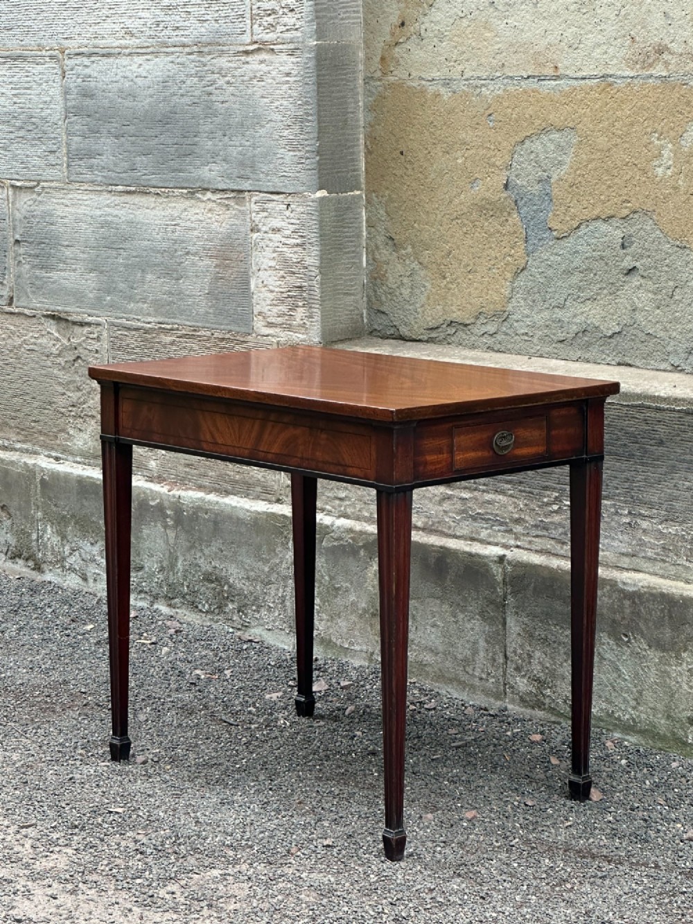 A George III mahogany side table with tapered legs, a flame mahogany veneered frieze, and a brass drawer pull. View IV