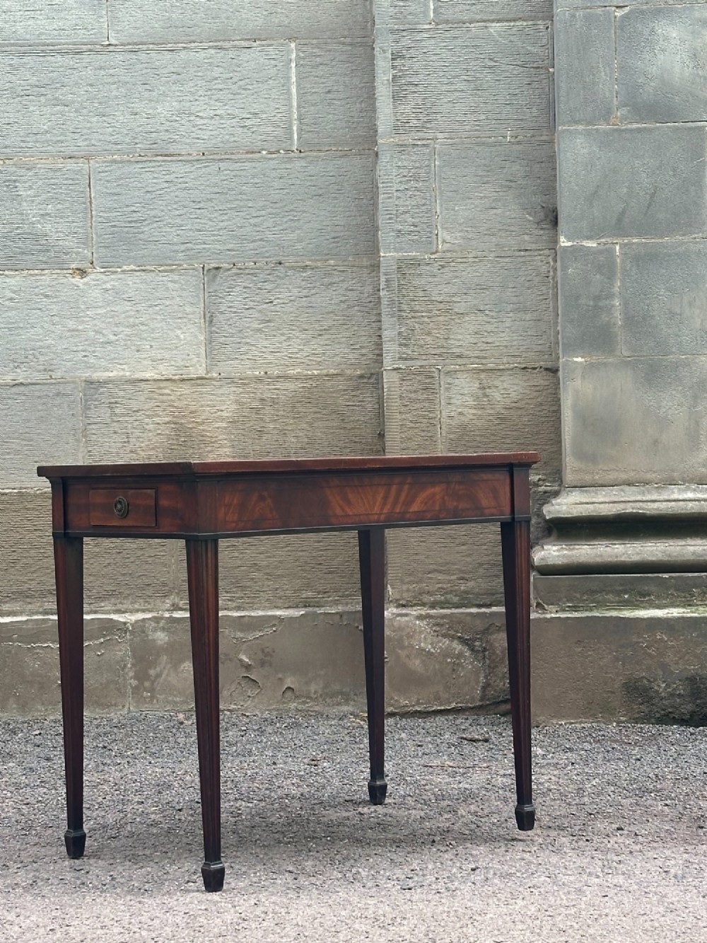 A George III mahogany side table with tapered legs, a flame mahogany veneered frieze, and a brass drawer pull. View VII