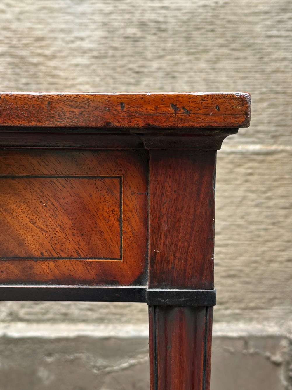 A George III mahogany side table with tapered legs, a flame mahogany veneered frieze, and a brass drawer pull. View X