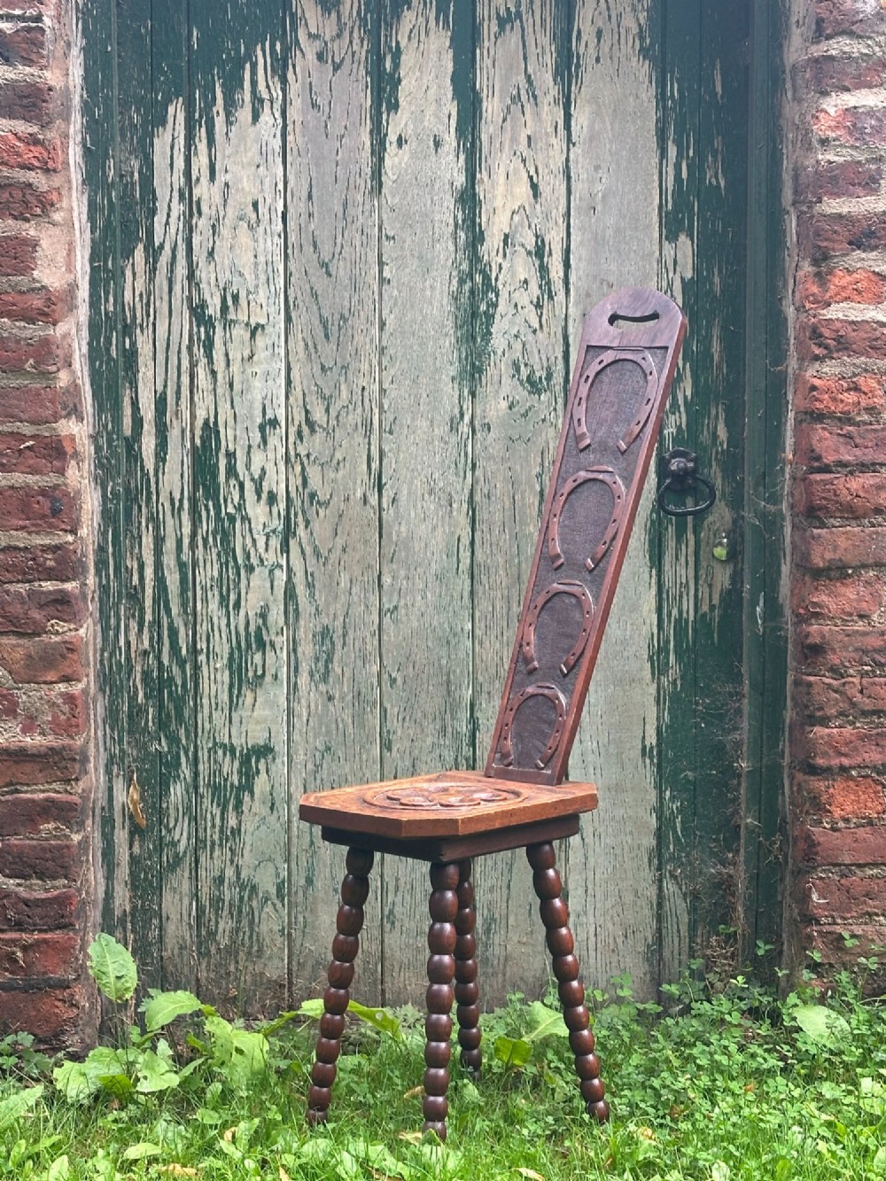 An Arts and Crafts carved wooden spinning stool featuring a tall narrow backrest, a relief-carved floral seat, and bobbin-turned legs. View VII