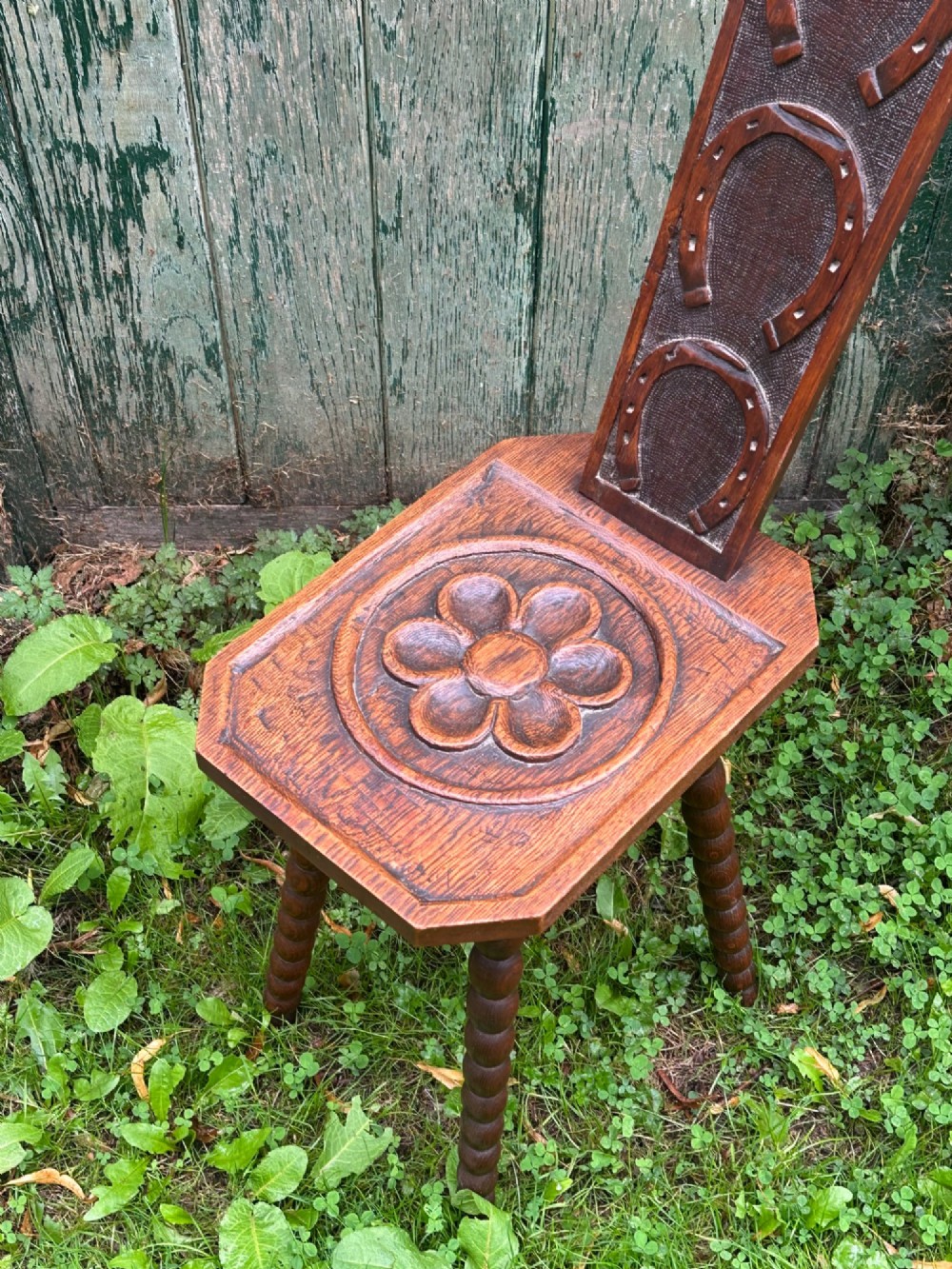 An Arts and Crafts carved wooden spinning stool featuring a tall narrow backrest, a relief-carved floral seat, and bobbin-turned legs. View VIII