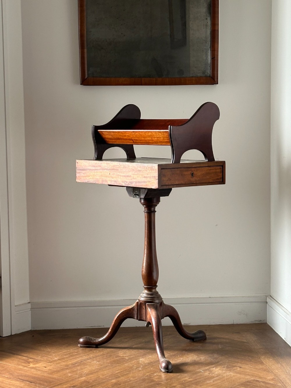 A late Victorian mahogany standing book trough featuring an upper angled trough, a small frieze drawer, turned pedestal stem, and tripod legs.