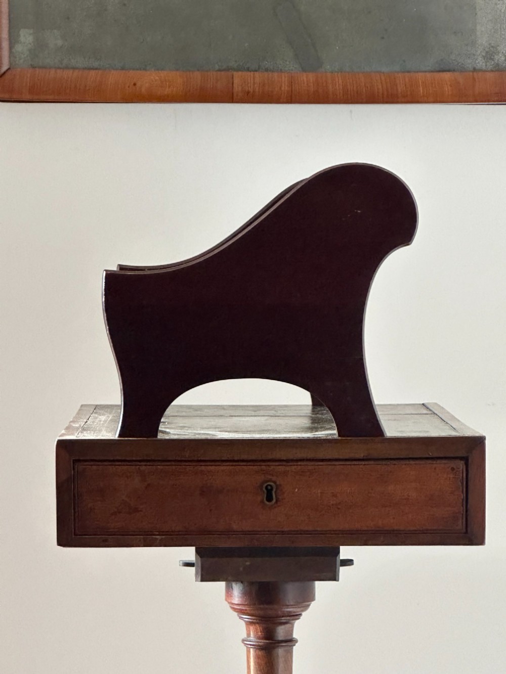 A late Victorian mahogany standing book trough featuring an upper angled trough, a small frieze drawer, turned pedestal stem, and tripod legs. View V
