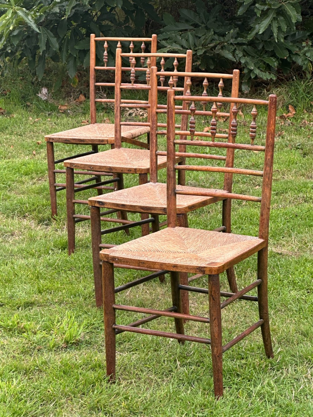 A set of four nineteenth-century beech Sussex chairs featuring turned spindle backrests and woven rush seats lined up outdoors. View II