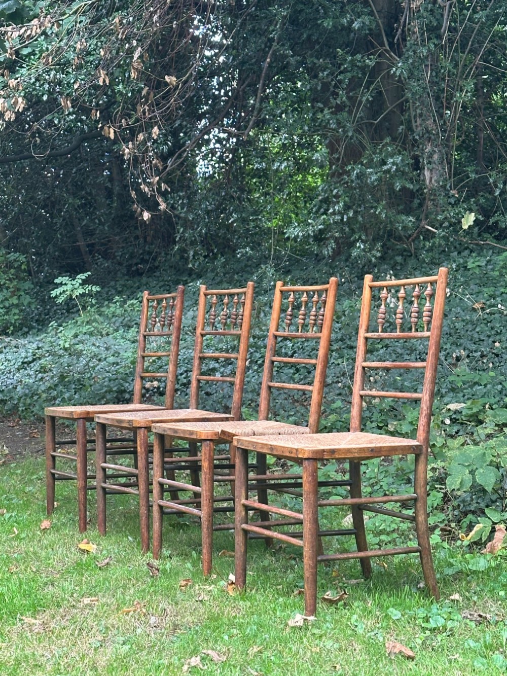A set of four nineteenth-century beech Sussex chairs featuring turned spindle backrests and woven rush seats lined up outdoors. View III