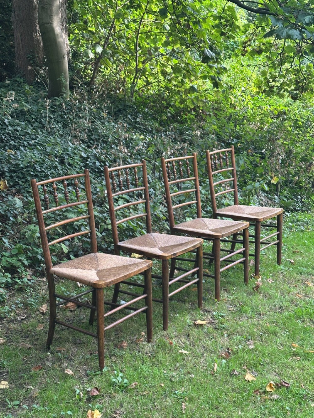 A set of four nineteenth-century beech Sussex chairs featuring turned spindle backrests and woven rush seats lined up outdoors. View V