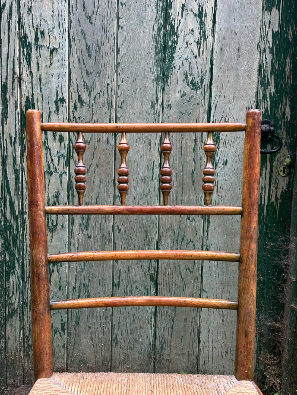A set of four nineteenth-century beech Sussex chairs featuring turned spindle backrests and woven rush seats lined up outdoors. View X
