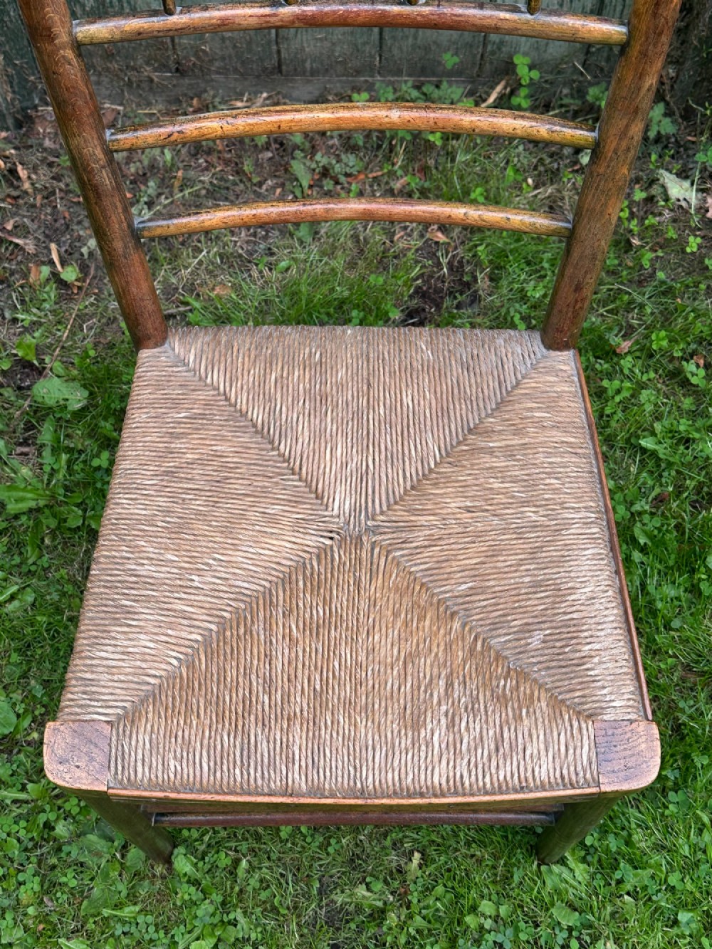 A set of four nineteenth-century beech Sussex chairs featuring turned spindle backrests and woven rush seats lined up outdoors. View XI