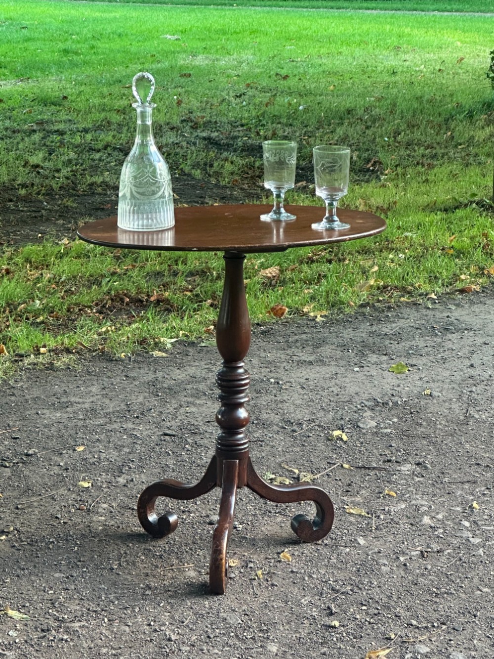 A George III mahogany tripod table featuring a circular top supported by a turned central stem and three scrolled legs. View III