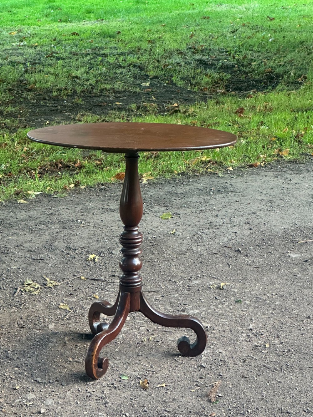 A George III mahogany tripod table featuring a circular top supported by a turned central stem and three scrolled legs.