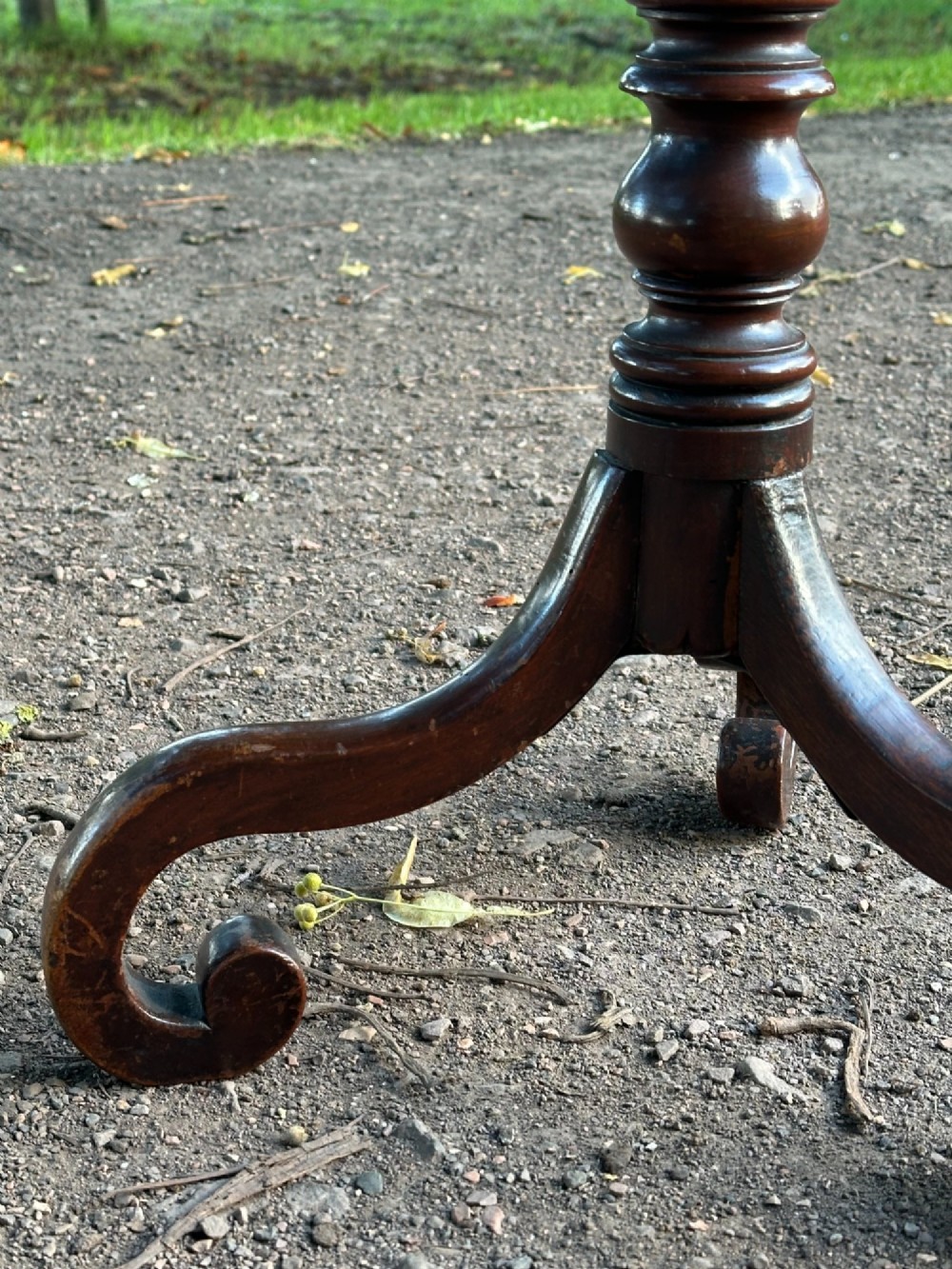 A George III mahogany tripod table featuring a circular top supported by a turned central stem and three scrolled legs. View VI