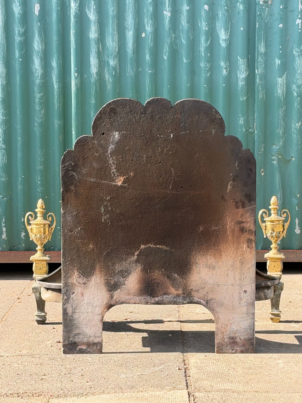 A late nineteenth-century George III style fire grate featuring an ornate cast iron fireback with scrollwork and decorative brass urn finials set on tapered brass legs. View II