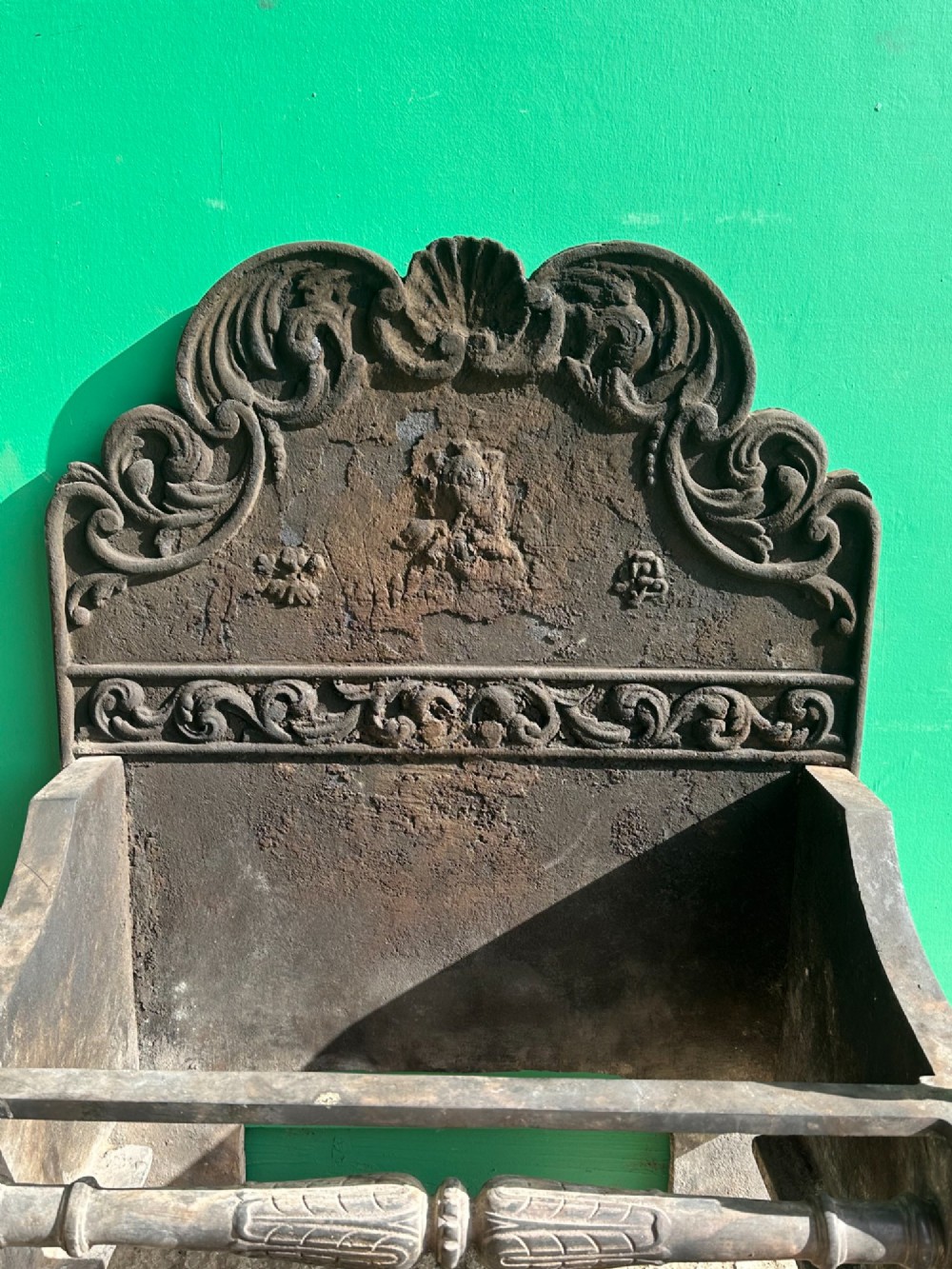 A late nineteenth-century George III style fire grate featuring an ornate cast iron fireback with scrollwork and decorative brass urn finials set on tapered brass legs. View IV