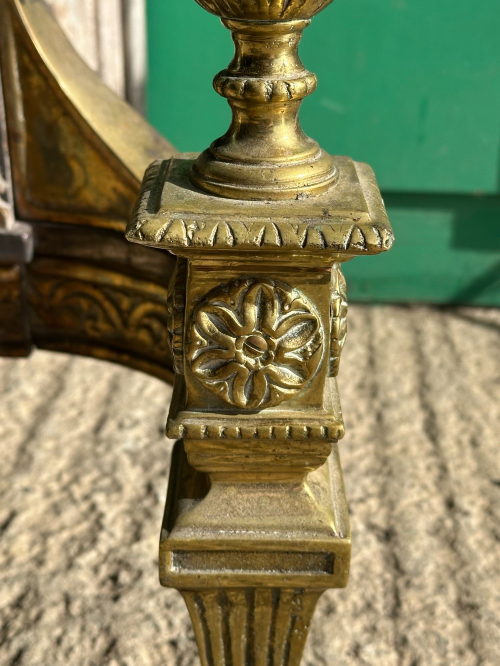 A late nineteenth-century George III style fire grate featuring an ornate cast iron fireback with scrollwork and decorative brass urn finials set on tapered brass legs. View V