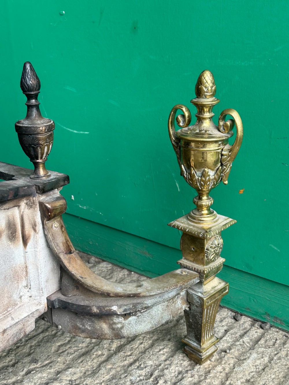 A late nineteenth-century George III style fire grate featuring an ornate cast iron fireback with scrollwork and decorative brass urn finials set on tapered brass legs. View XI