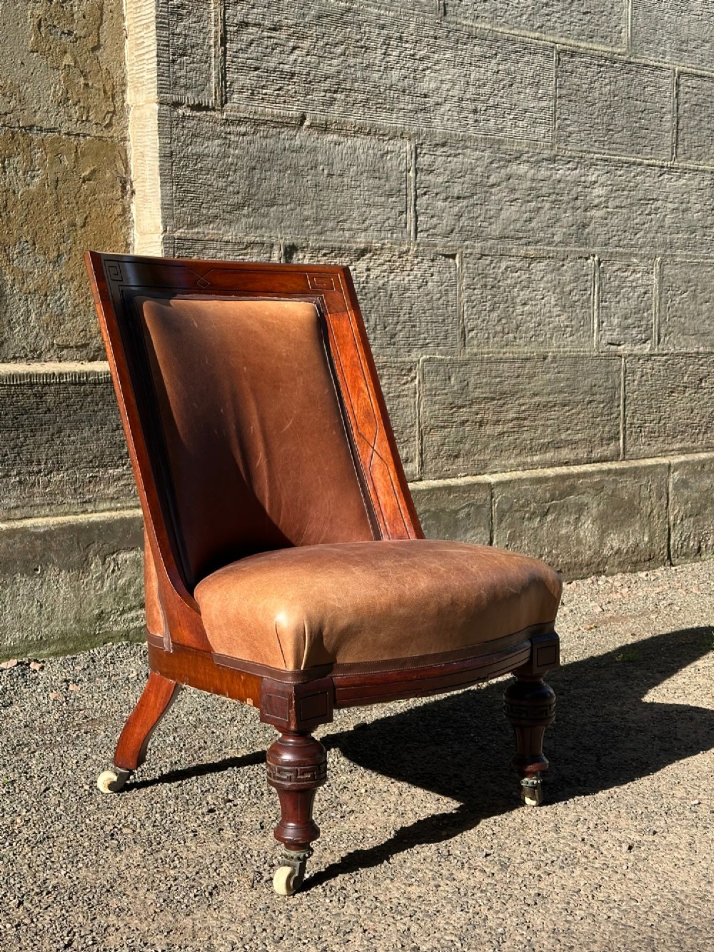 A pair of nineteenth-century Greek Revival mahogany armchairs upholstered in warm brown leather with turned front legs on castors and incised geometric detailing. View II
