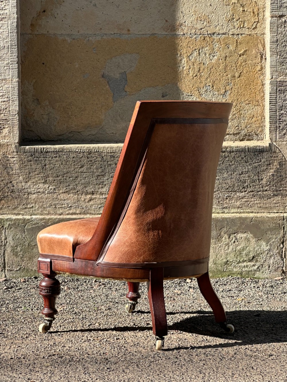 A pair of nineteenth-century Greek Revival mahogany armchairs upholstered in warm brown leather with turned front legs on castors and incised geometric detailing. View III