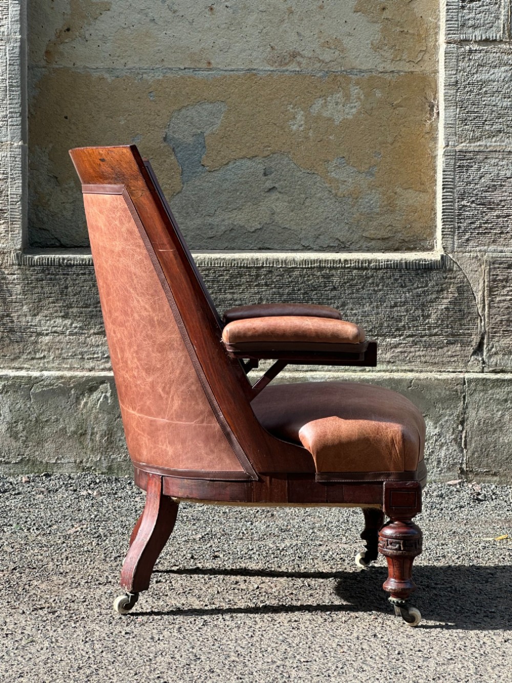 A pair of nineteenth-century Greek Revival mahogany armchairs upholstered in warm brown leather with turned front legs on castors and incised geometric detailing. View V