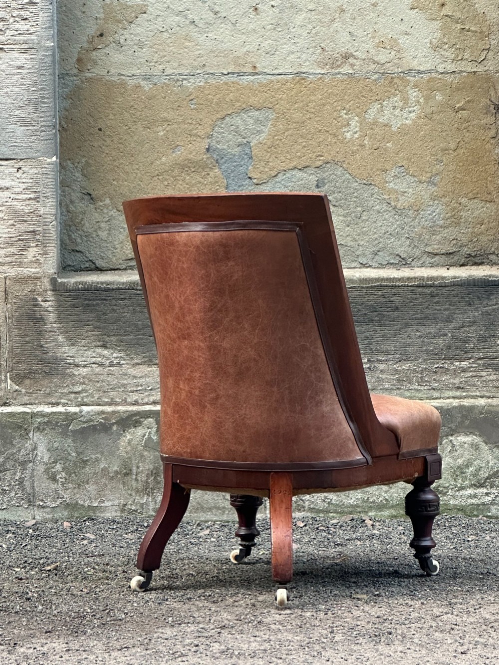 A pair of nineteenth-century Greek Revival mahogany armchairs upholstered in warm brown leather with turned front legs on castors and incised geometric detailing. View VIII