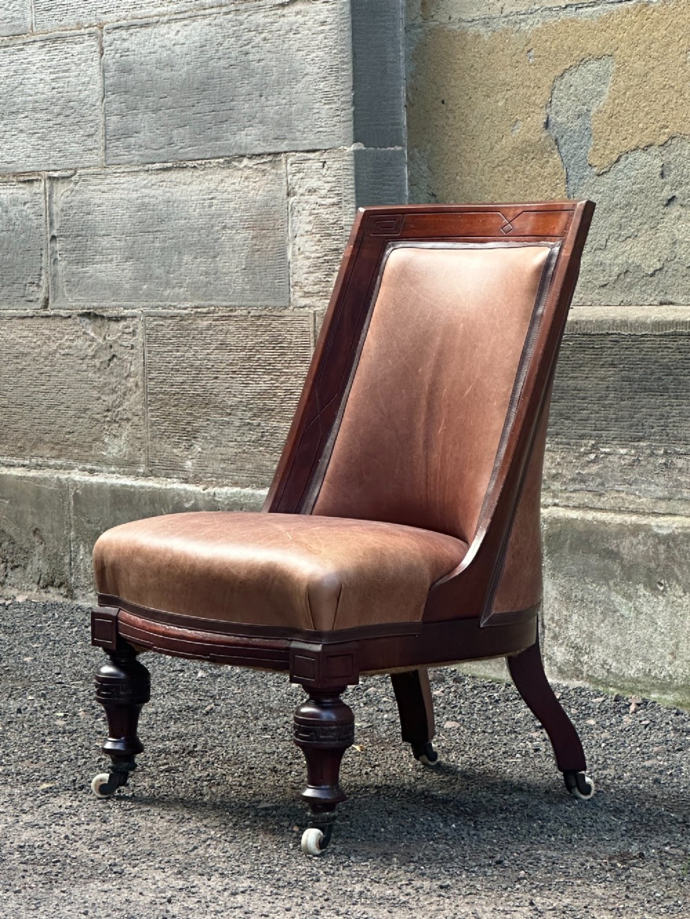A pair of nineteenth-century Greek Revival mahogany armchairs upholstered in warm brown leather with turned front legs on castors and incised geometric detailing. View IX