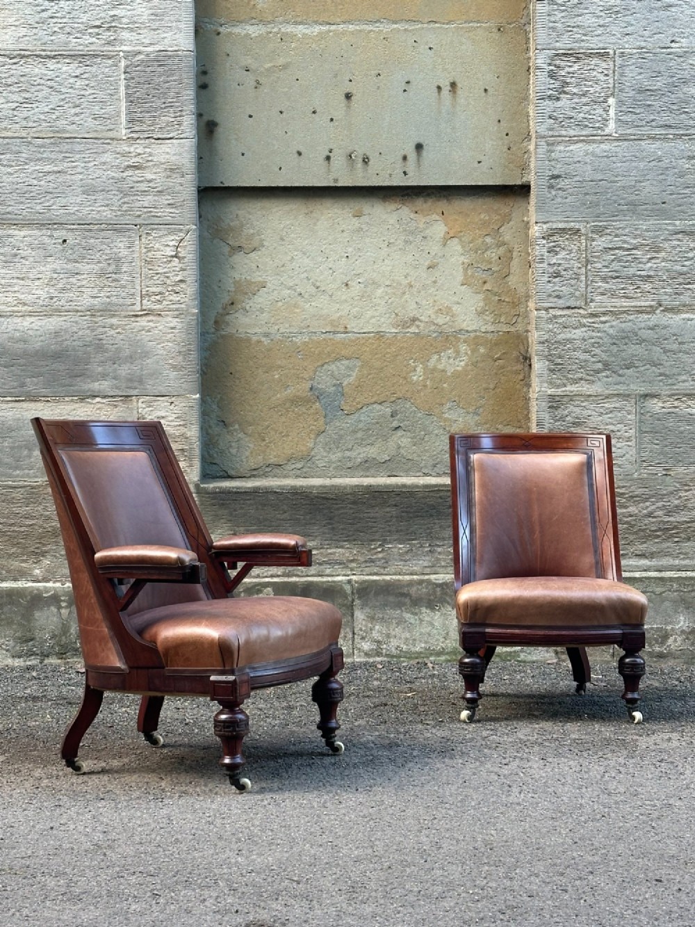 A pair of nineteenth-century Greek Revival mahogany armchairs upholstered in warm brown leather with turned front legs on castors and incised geometric detailing. View X