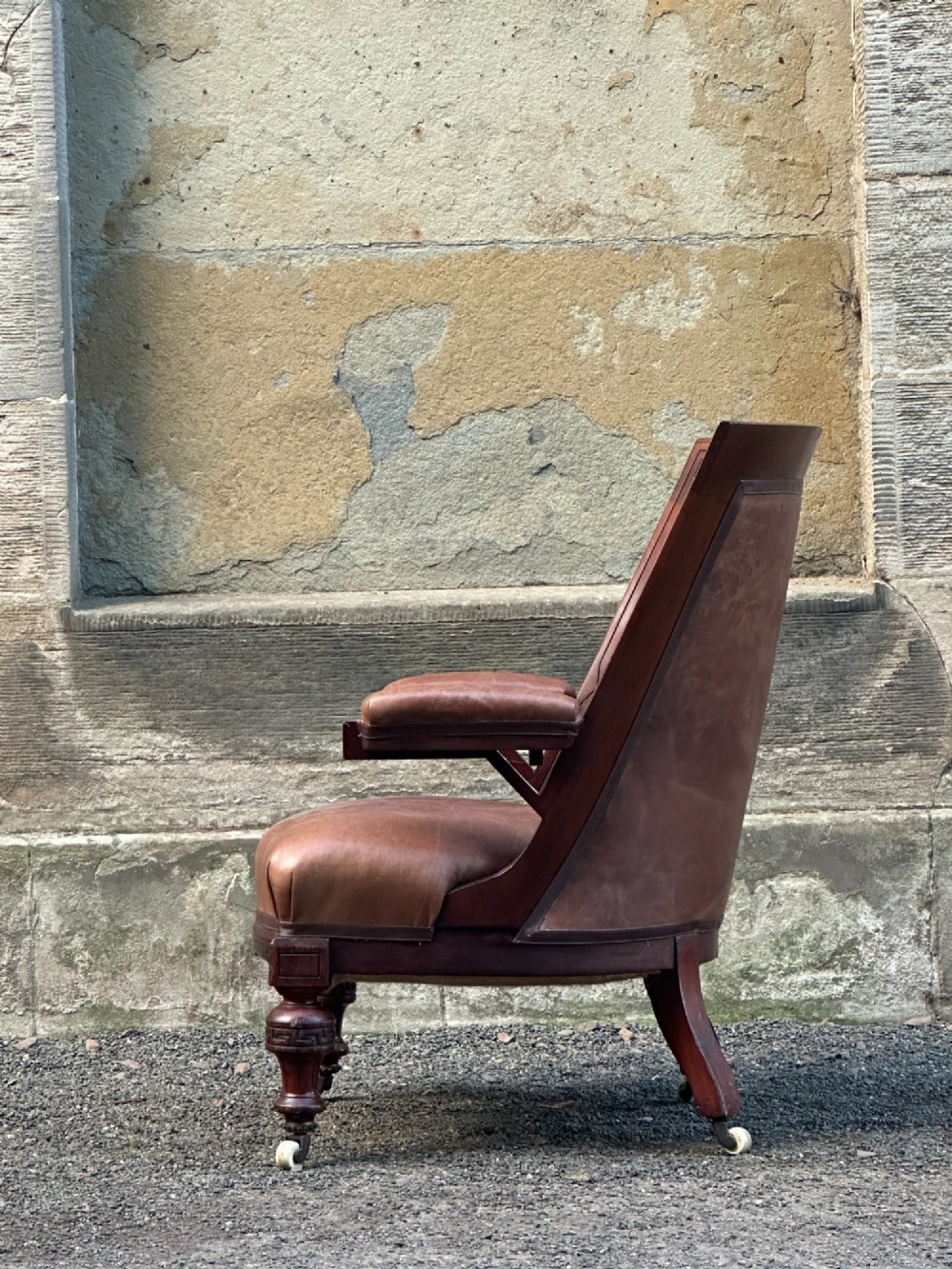 A pair of nineteenth-century Greek Revival mahogany armchairs upholstered in warm brown leather with turned front legs on castors and incised geometric detailing. View XI